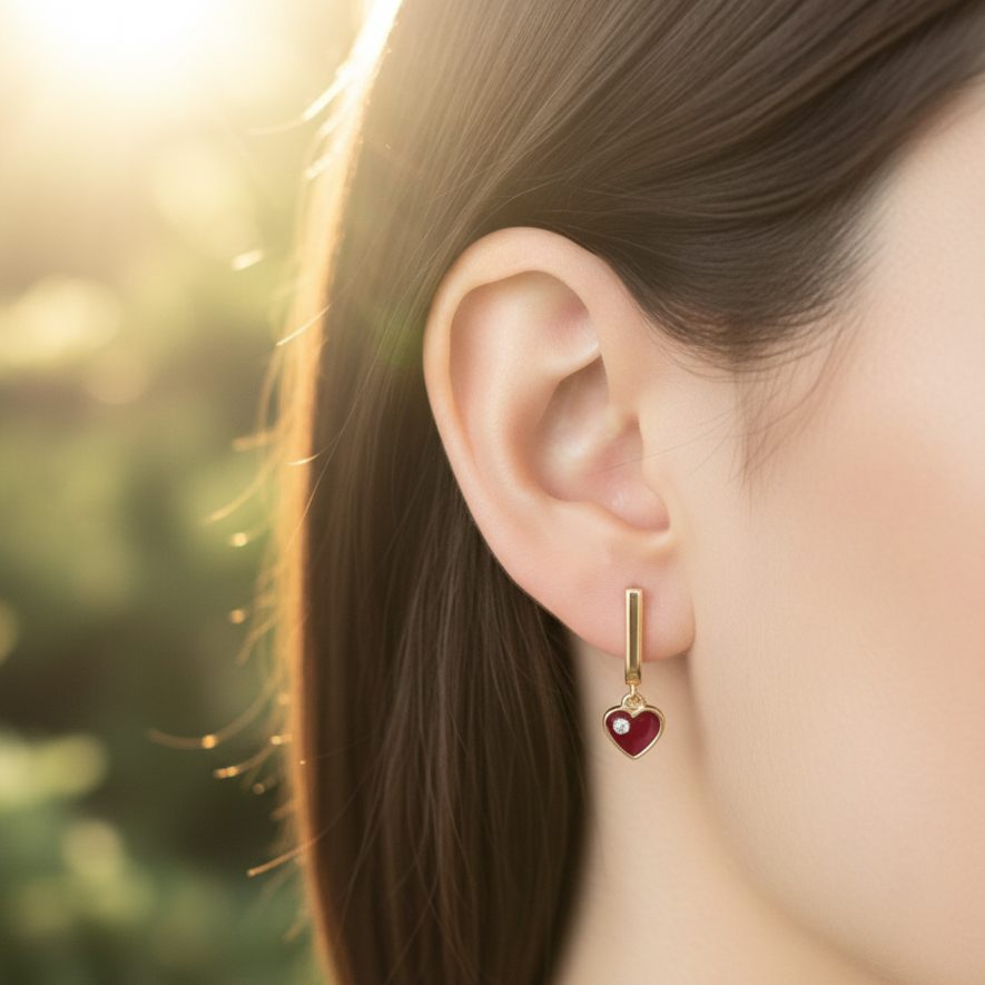 Gold earring with a red heart charm worn by a person outdoors.