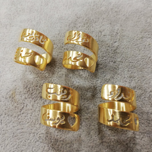 Five gold-toned split cuff rings with Arabic calligraphy engraved on the bands, arranged on a textured gray surface.