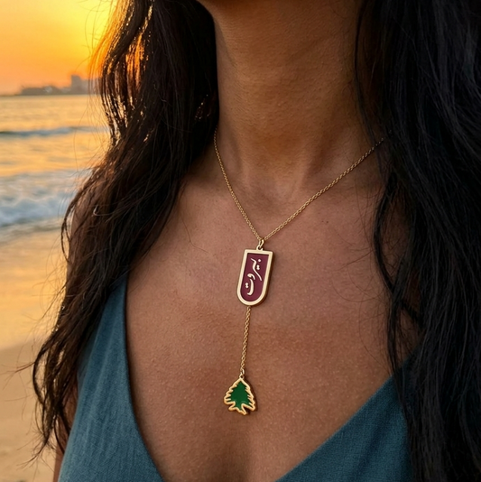 Person wearing a beirut necklace with a cedar charm on a beach at sunset