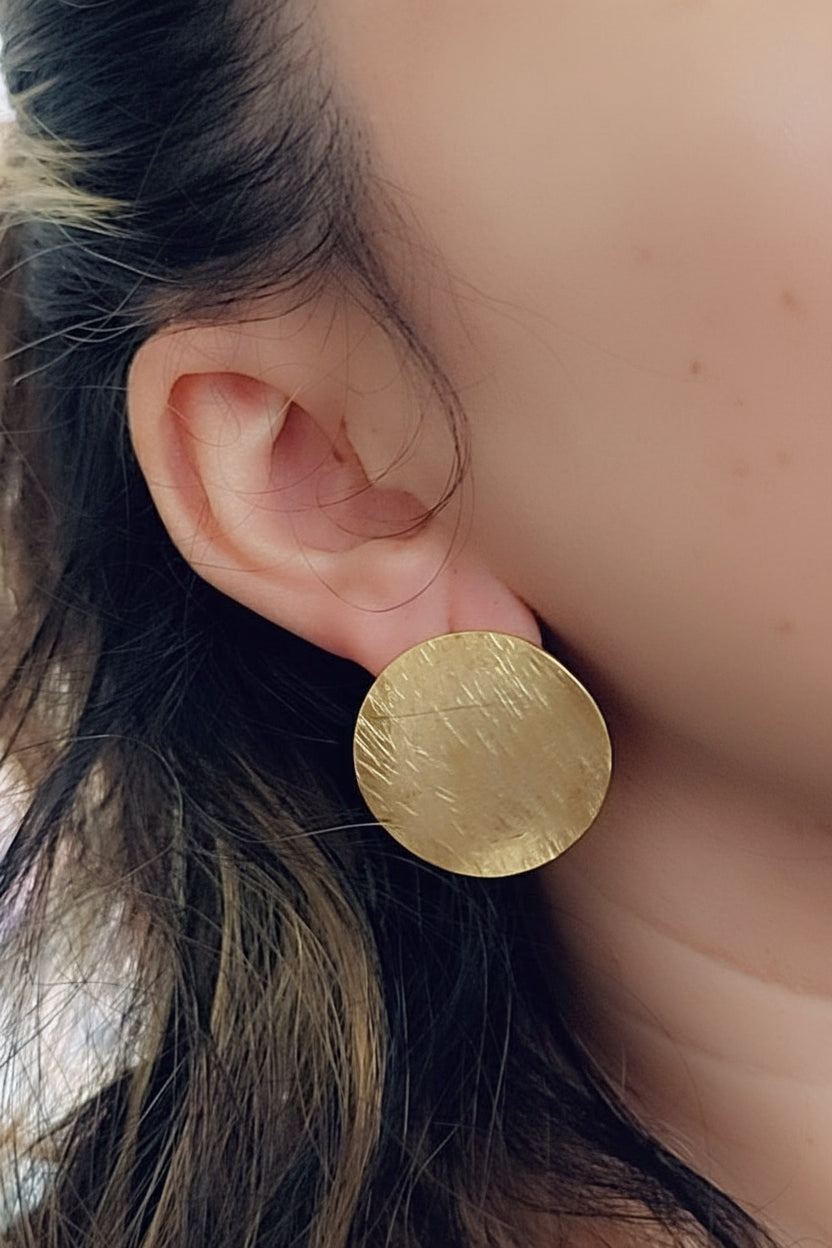 Close-up of a person wearing a gold round earring.