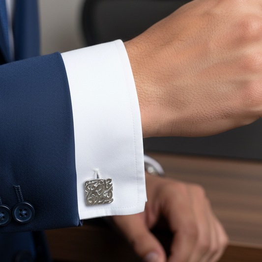 Close-up of a person wearing a navy suit with a white shirt and silver arabic calligraphy name cufflinks.