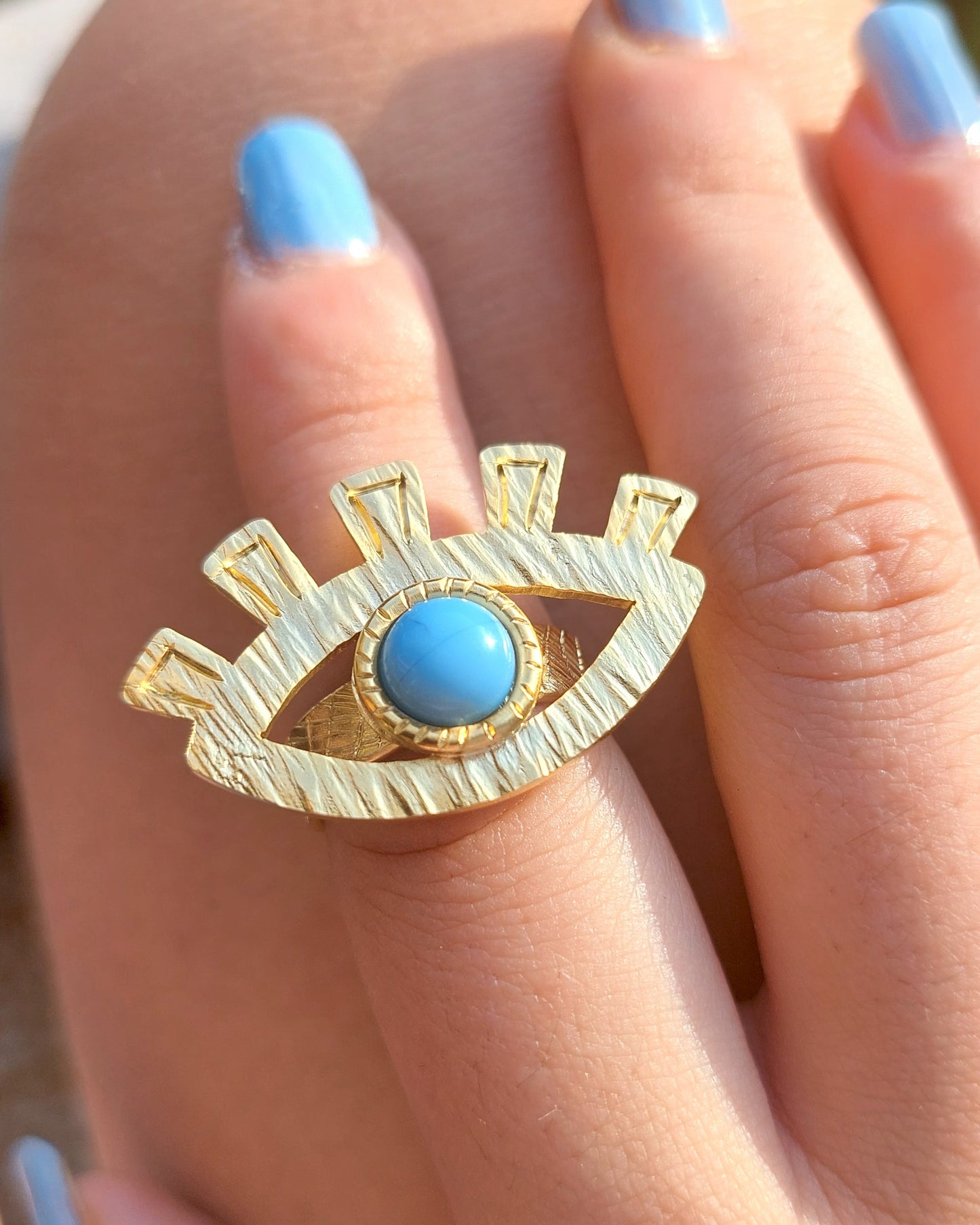 Gold ring with a blue stone on a person's finger with light blue nail polish.