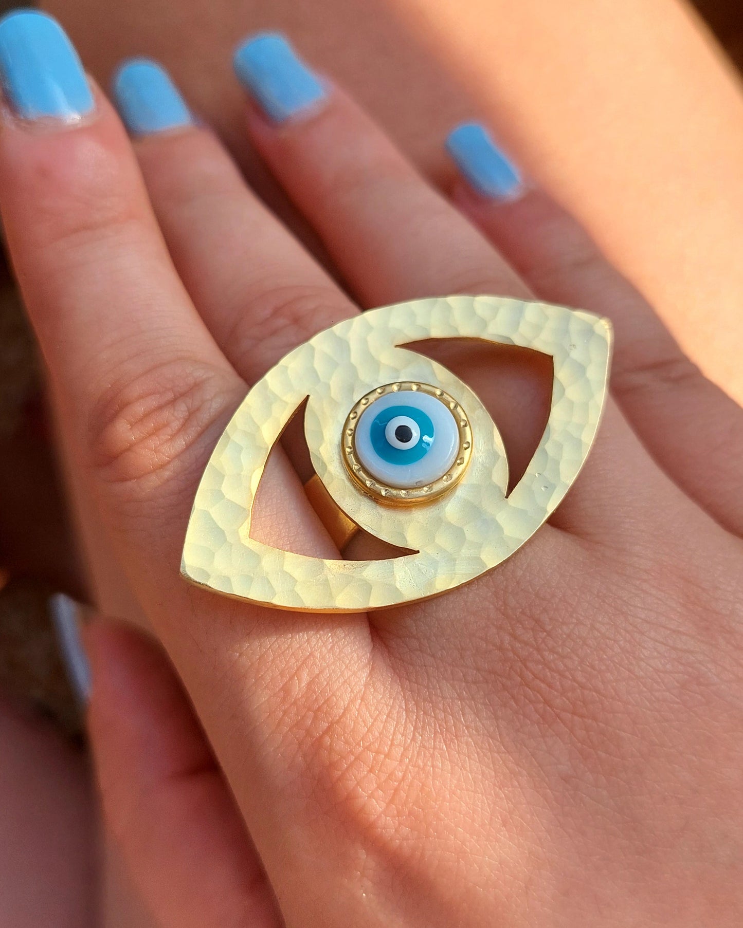 Hand wearing a gold eye-shaped ring with a white evil eye.