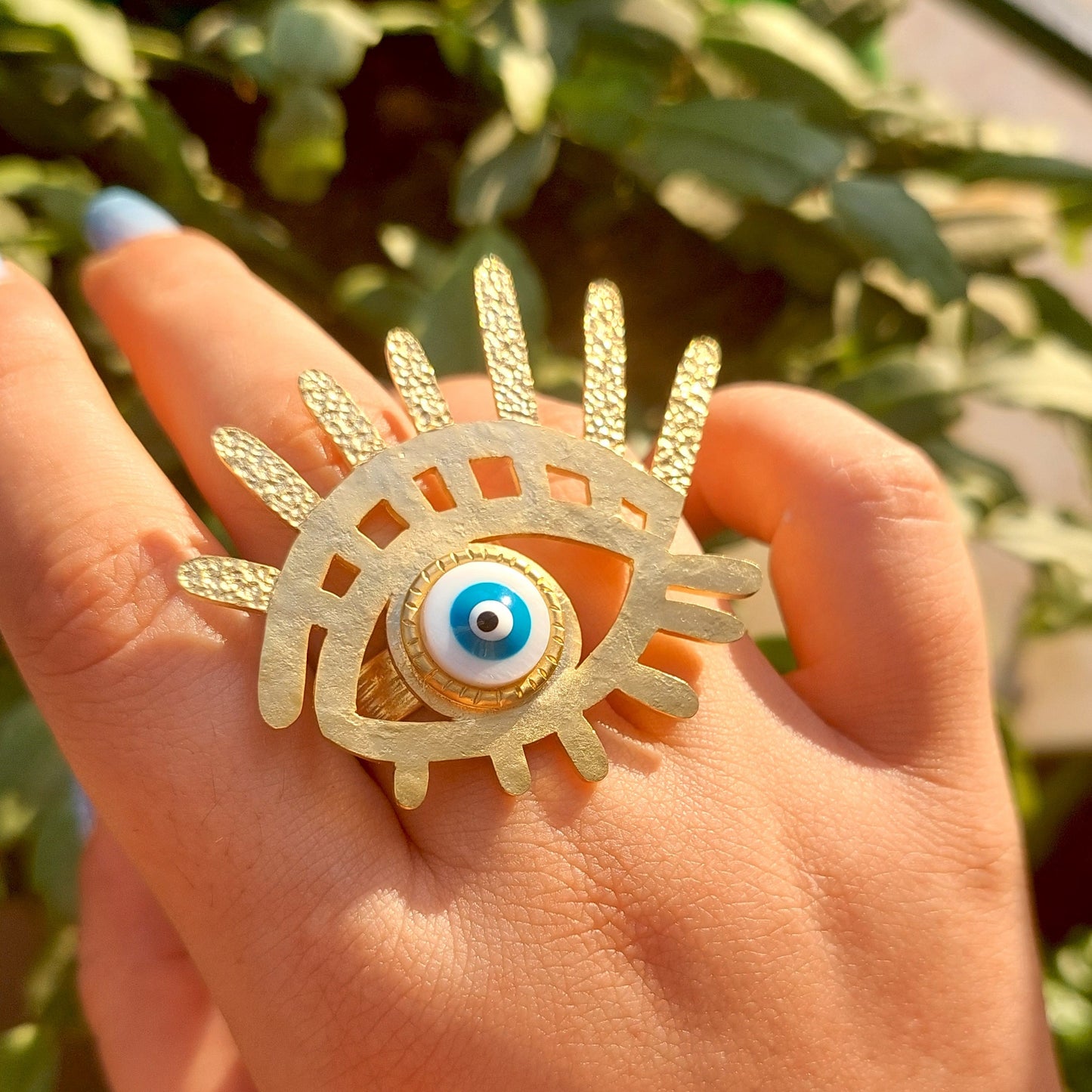 Gold ring with eye design held in a hand against a blurred green background