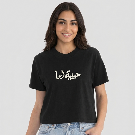 Woman wearing a black t-shirt with Arabic text habibet ema on a white background