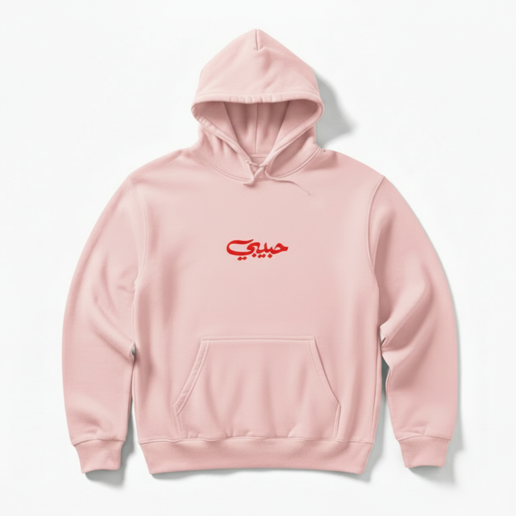 Pink hoodie with red habibi written in arabic on a white background