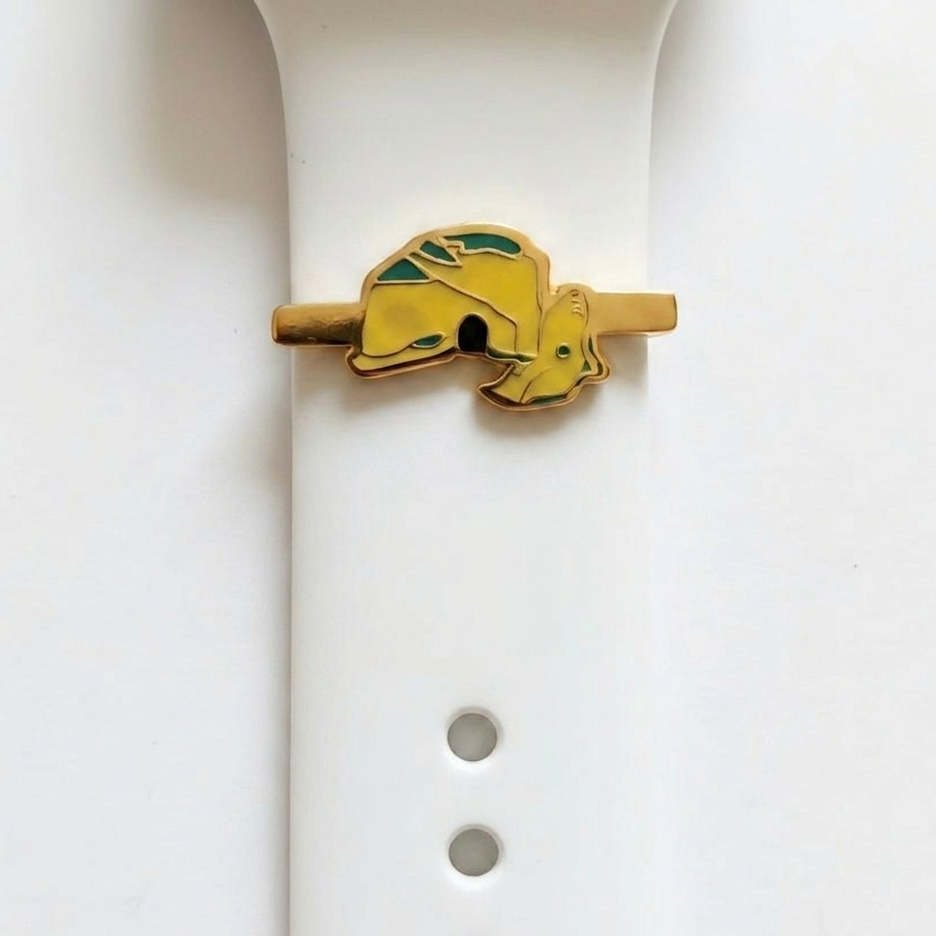 Yellow and gold raouche shaped watch charm on a white watch rubber band on a white background