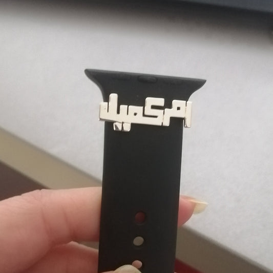 Black watch strap with silver arabic name held by a hand on a blurred background