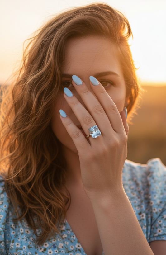 Woman with a blue ring on her finger, holding her hand to her face against a blurred natural background