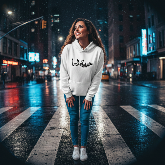 Woman in a white hoodie with Arabic text standing on a city street at night.