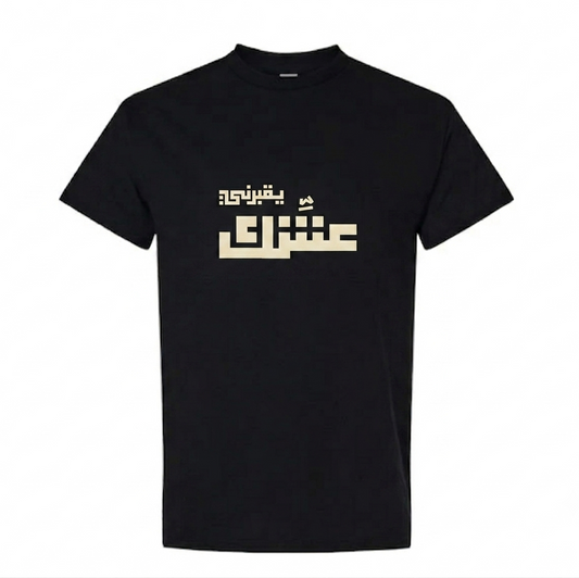 A black short-sleeve crewneck t-shirt featuring a stylized beige Arabic text graphic yo2borni 3eshik printed across the chest, displayed on a solid white background.