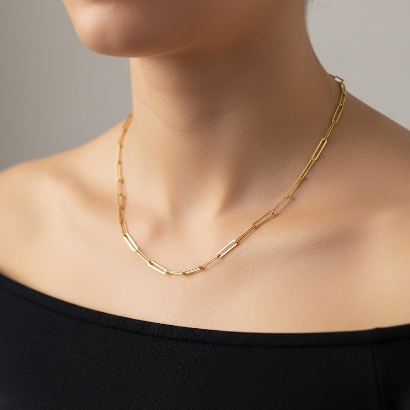 Gold chain necklace worn by a person against a neutral background