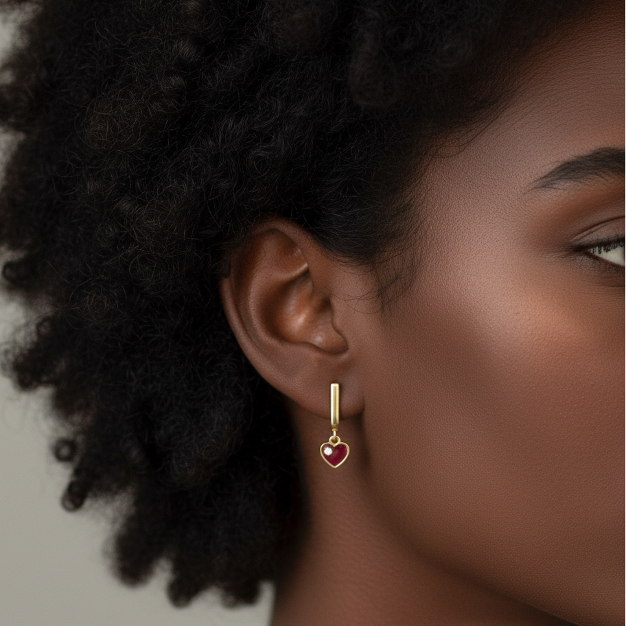 Close-up of a person wearing gold earrings with a heart design on a neutral background