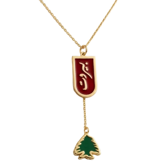 Gold beirut necklace with a red enamel and green cedar charm design on a white background