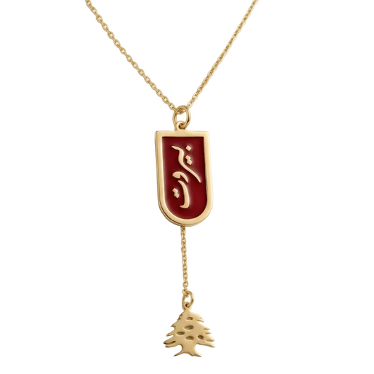 Gold necklace with a red beirut pendant and cedar charm on a white background