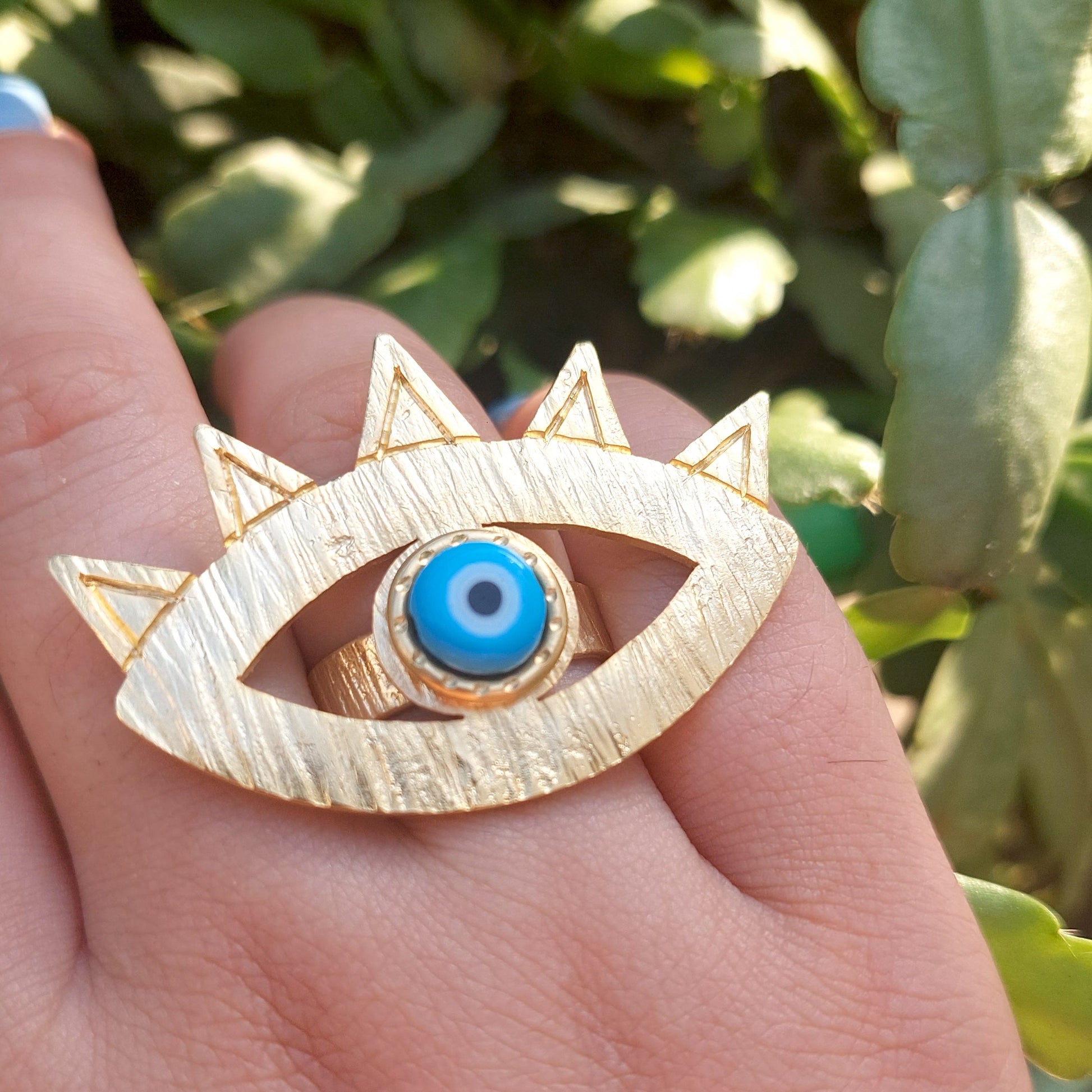 ring gold with blue evil eye on a had with blurred greens
