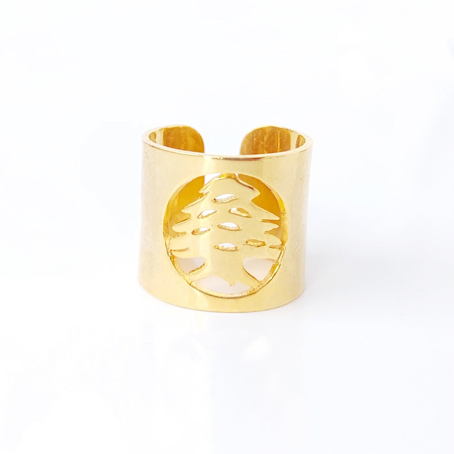 A gold-toned metal cuff ring featuring a circular cutout with a stylized tree design, set against a plain white background.