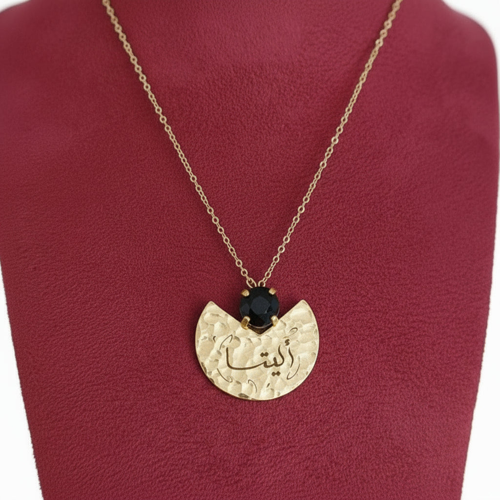 Gold necklace with a pendant featuring a black gemstone on a red cushion.