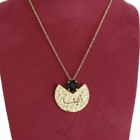 Gold necklace with a pendant featuring a black gemstone on a red cushion.
