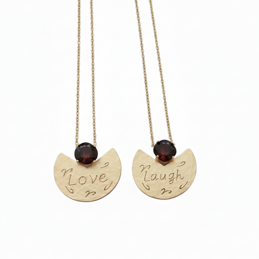 Two gold necklaces with engraved words 'Love' and 'Laugh' on a white background