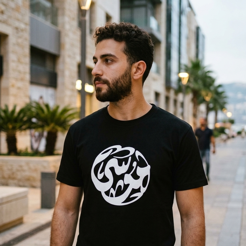 Man wearing a black t-shirt with a white logo on a city street.