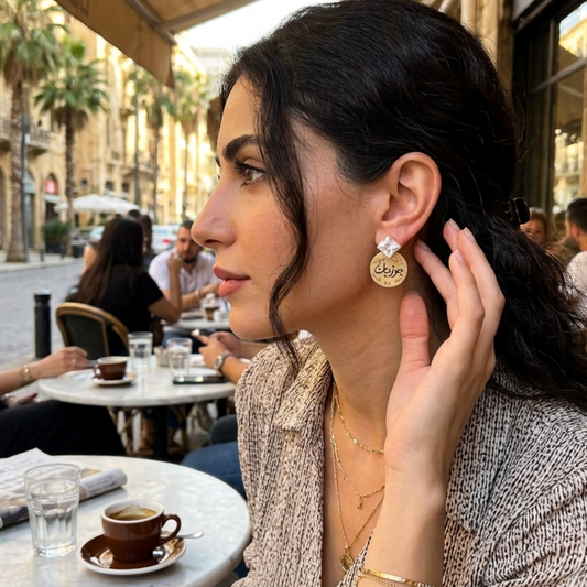 Woman sitting at an outdoor cafe table with a cup of coffee, wearing earrings and a bracelet.