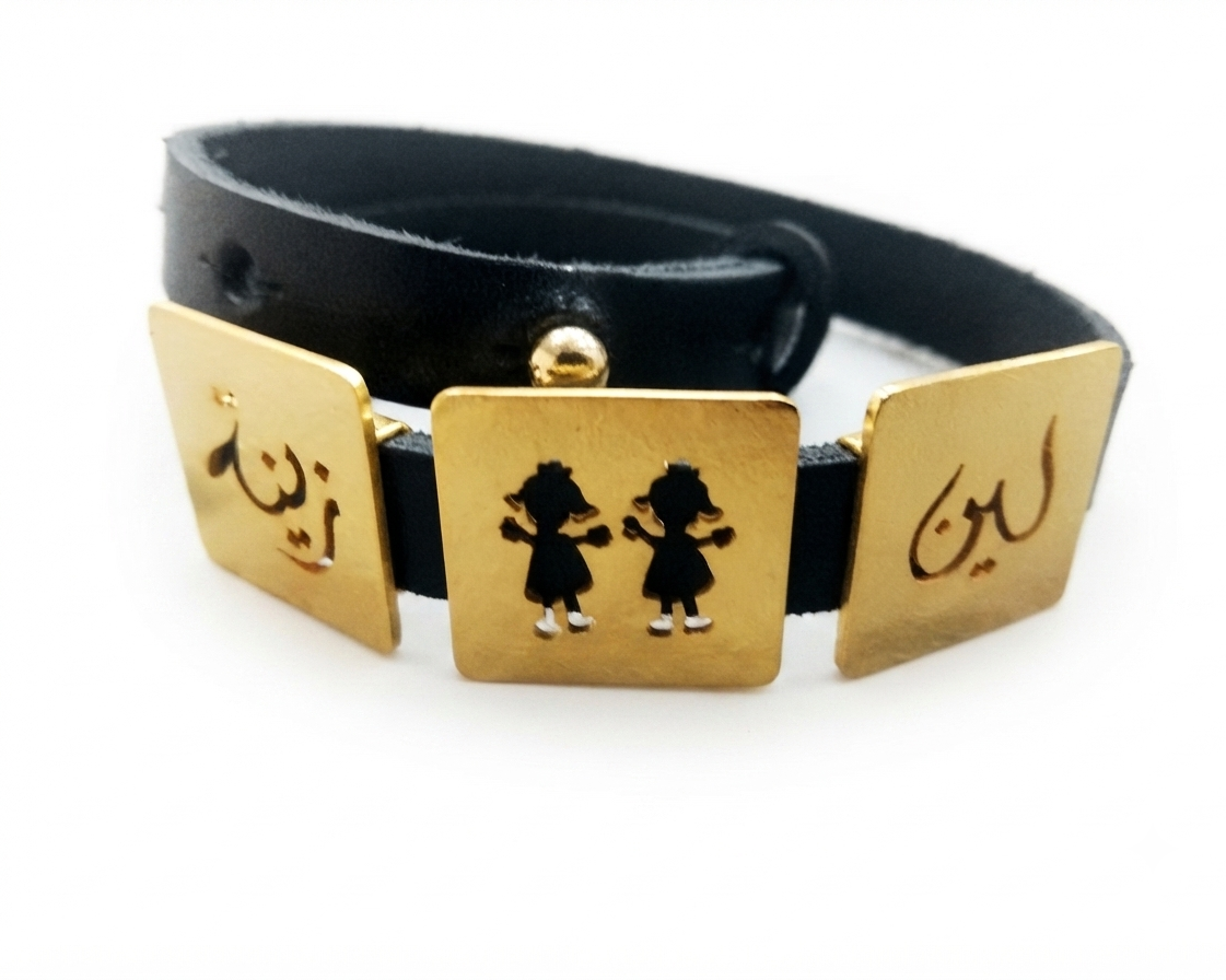 A black leather bracelet with three gold-tone square plates featuring black engravings, including Arabic calligraphy and two small child girl silhouettes, shown on a white background.