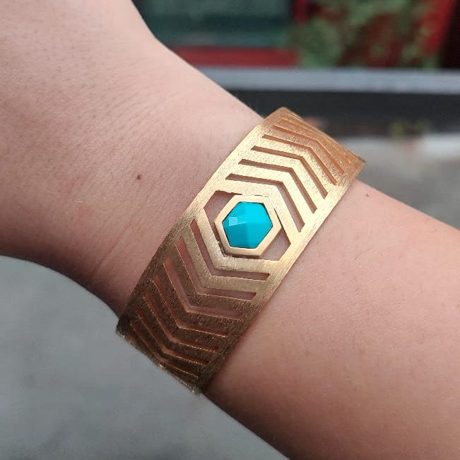 Gold bracelet with a blue gemstone on a wrist against a blurred background