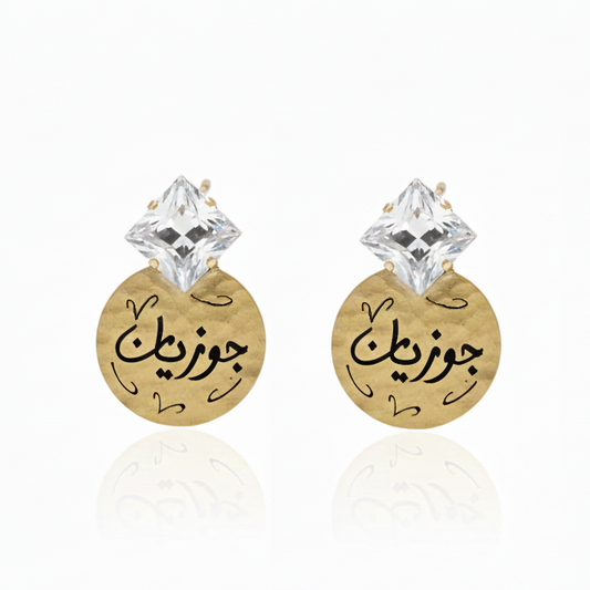 Gold earrings with Arabic text and clear square swarovski crystal on a white background