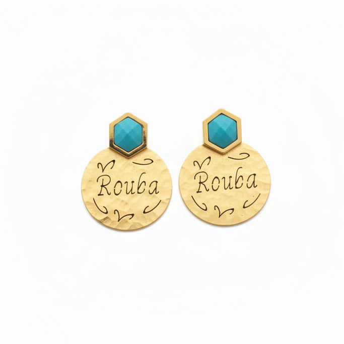 Gold earrings with turquoise stones and 'Rouba' engraving in a black box held by a hand.