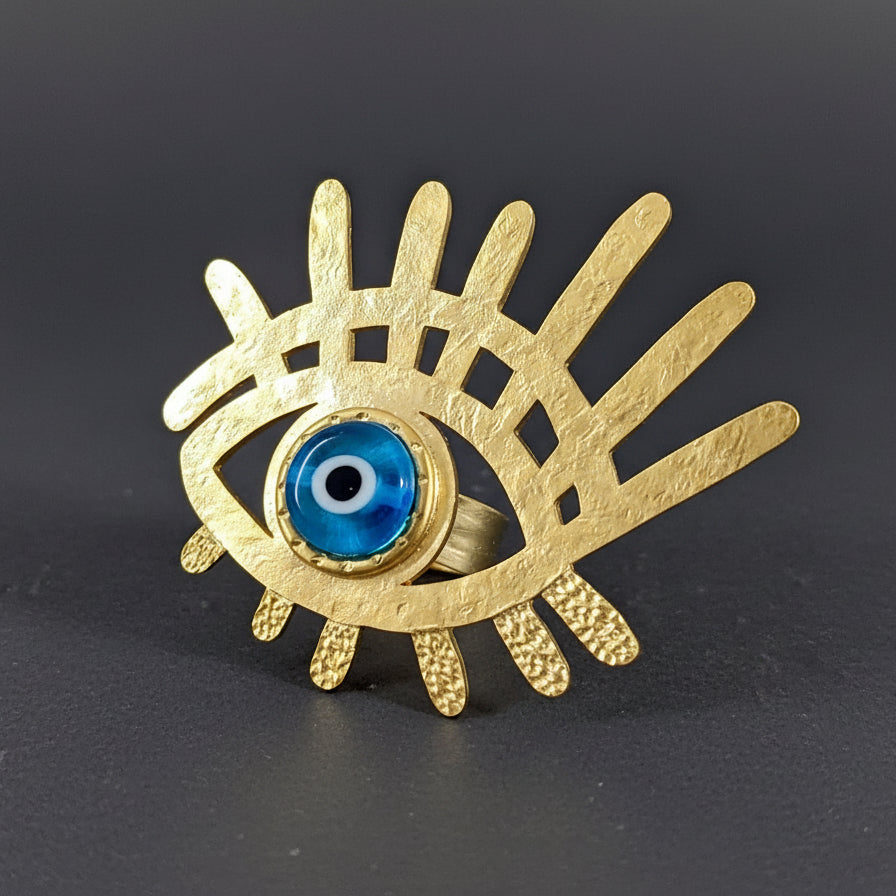 Gold eye-shaped ring with a blue center on a white background