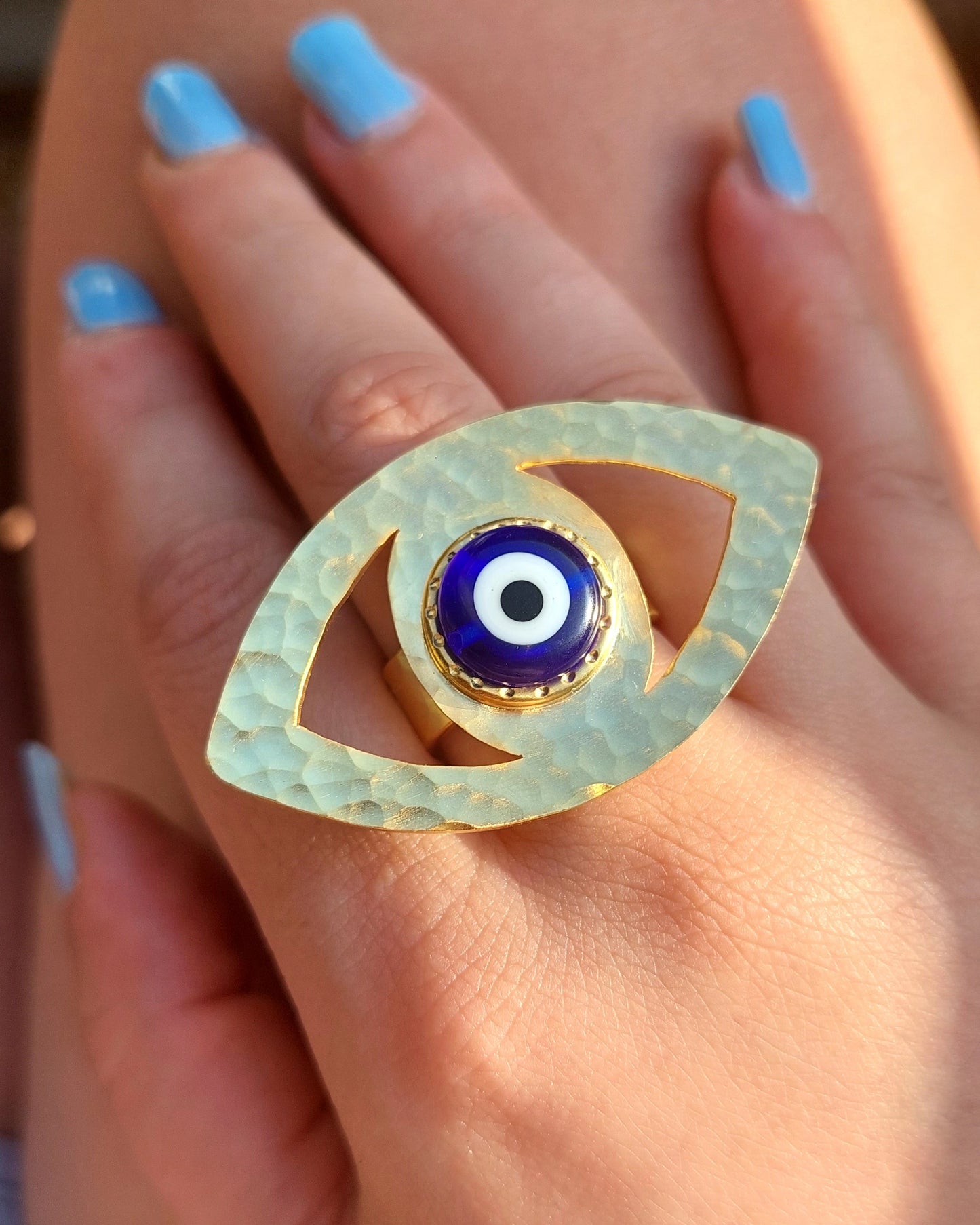 Gold eye-shaped ring with a blue center on a hand with light blue nail polish.