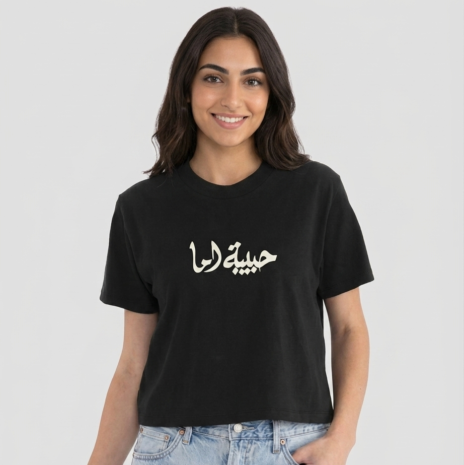 Woman wearing a black t-shirt with Arabic text habibet ema on a white background