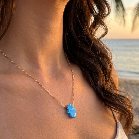 Woman wearing a blue hamsa necklace on a beach at sunset