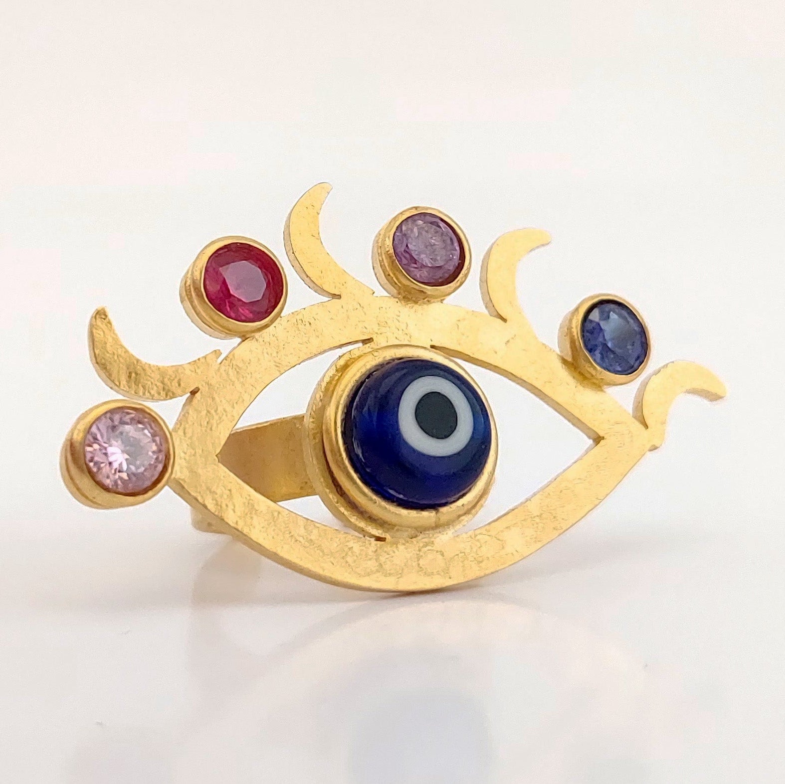 Gold ring with eye design and colored gemstones on a light background