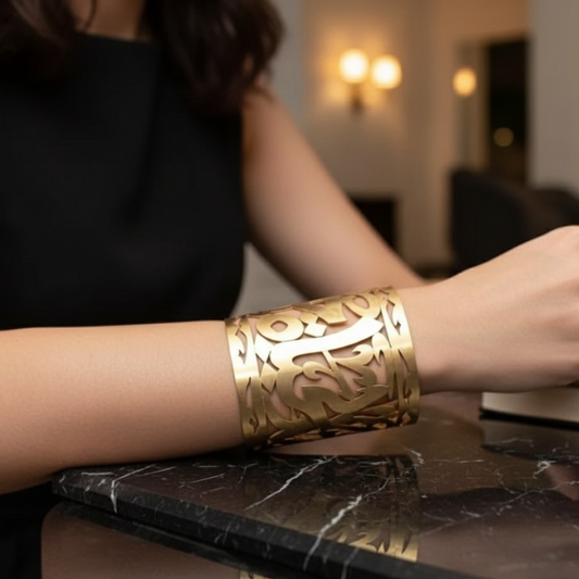 Gold cuff bracelet with intricate cut-out design on a womans hand sitting at the bar