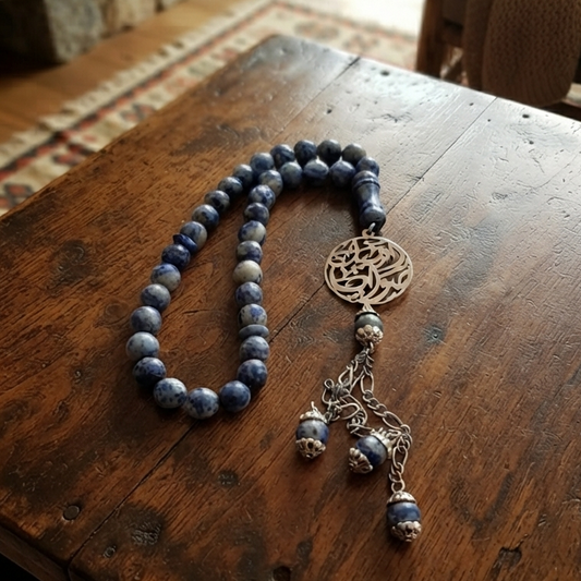 A beaded necklace with dark blue-gray round beads, a silver filigree centerpiece, and dangling silver charms resting on a rustic wooden table in a home interior.