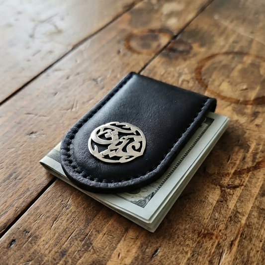 A black leather money clip with a silver-toned circular logo emblem, holding a stack of cash, resting on a rustic wooden table.