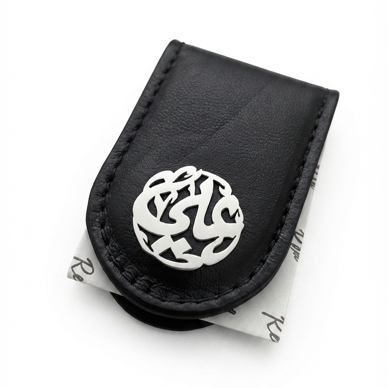 A black leather money clip featuring a silver-tone metal circular clasp with intricate Arabic calligraphy, displayed on a clean white background.