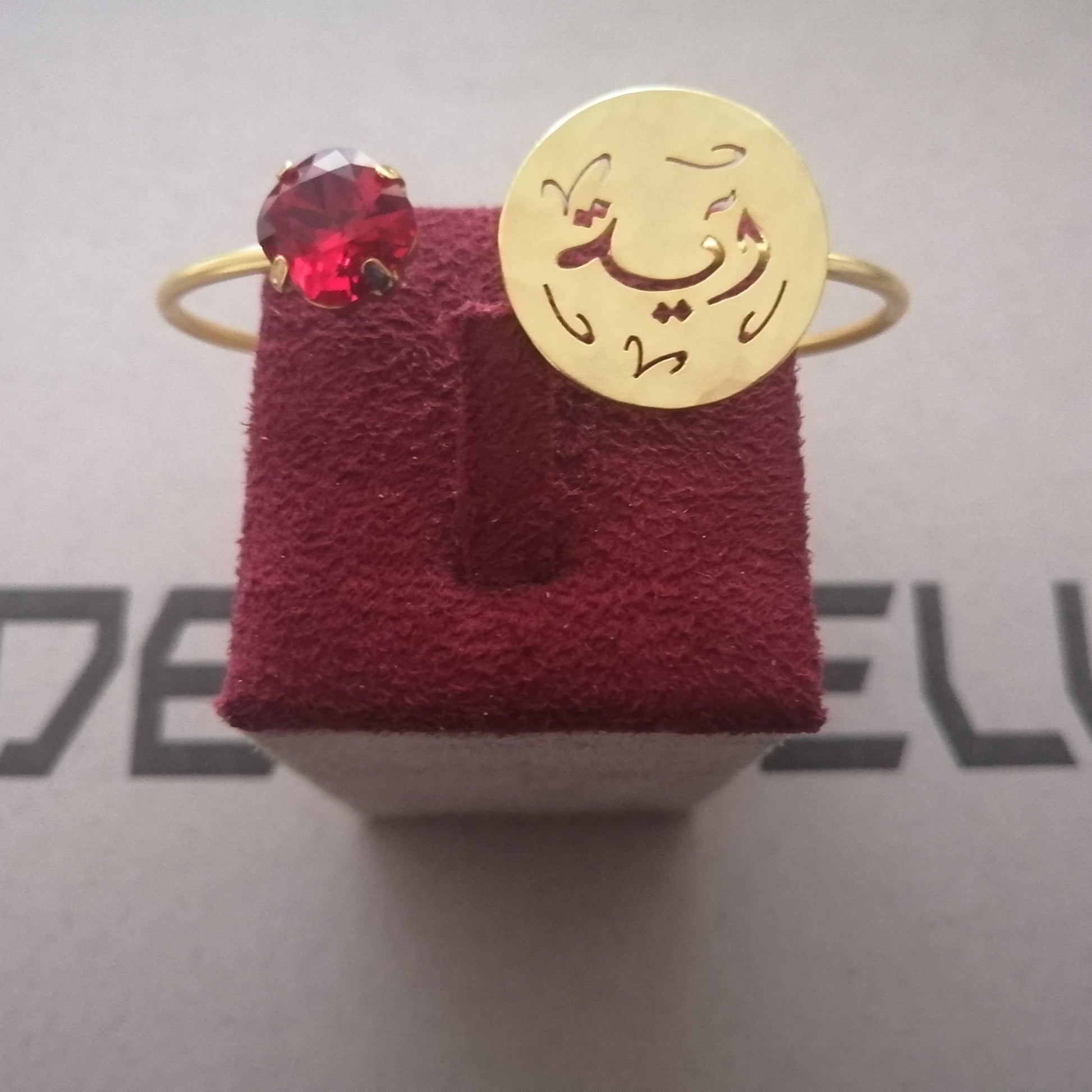 A gold bracelet hammered gold disc on the band with Arabic calligraphy engraved on it, alongside a small dark gemstone cluster.