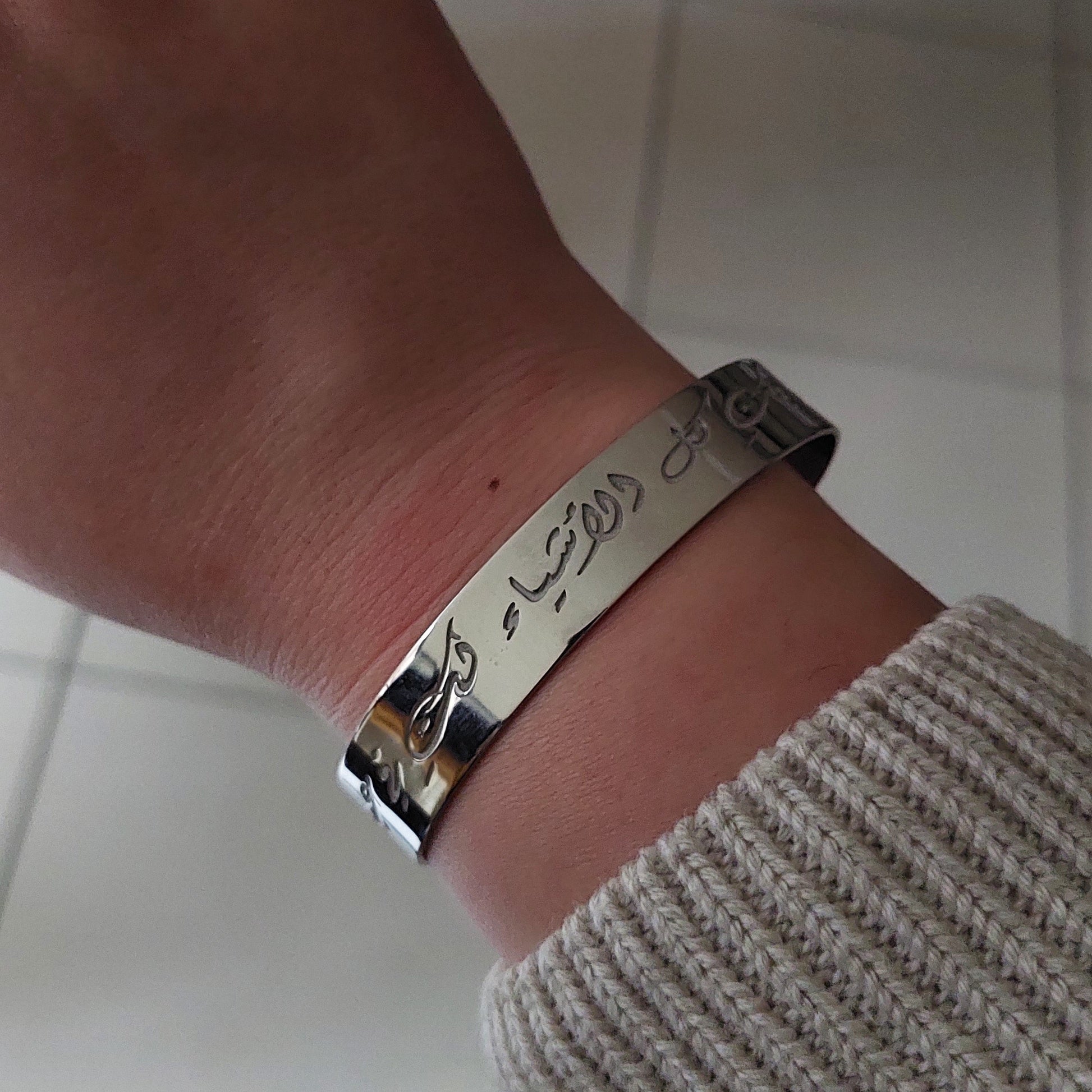 Close-up of a wrist wearing a silver bracelet with engraved text on a tiled floor background.