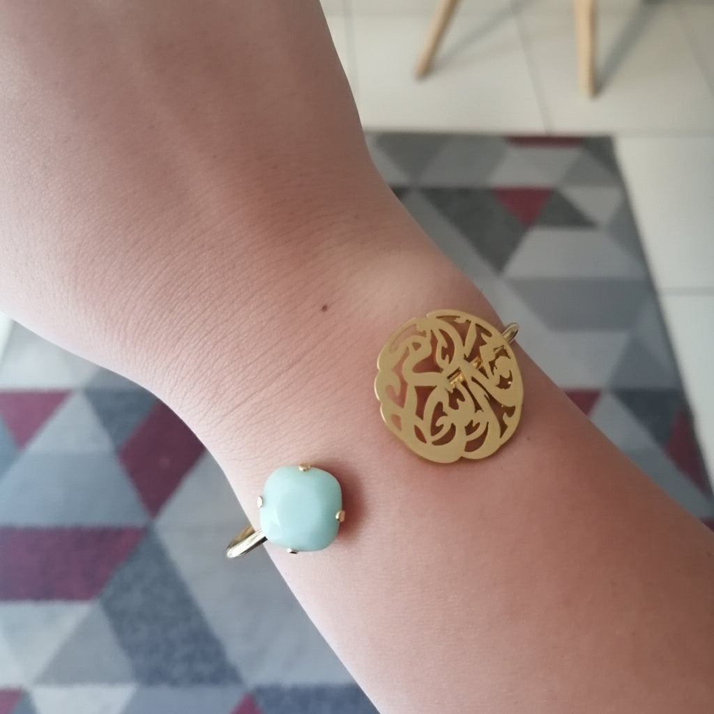 Gold bracelet with a turquoise bead on a wrist, with a geometric patterned floor in the background.