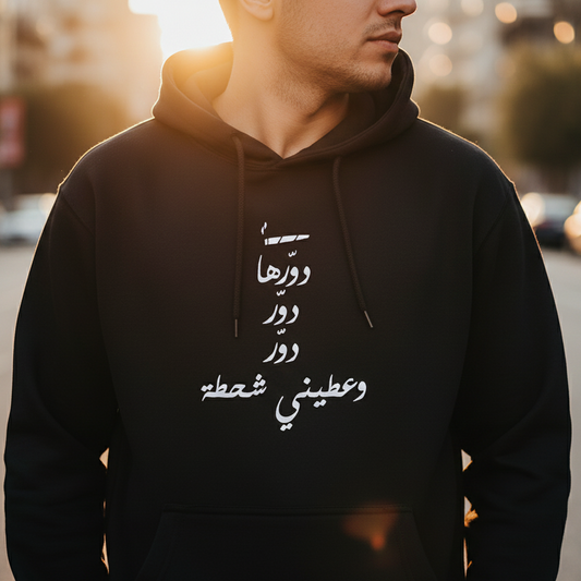 Person wearing a black hoodie with Arabic text on a blurred street background
