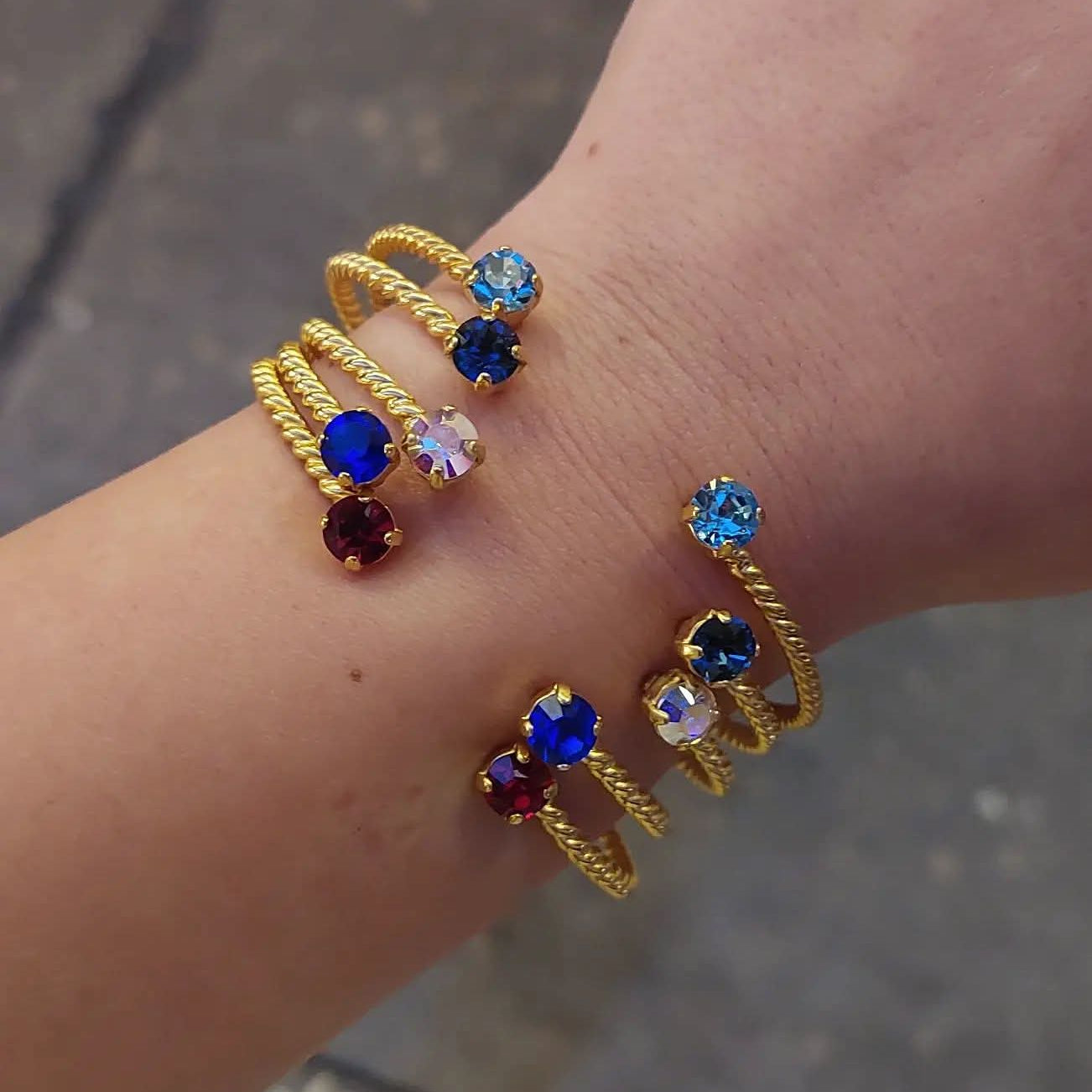 Gold bracelets with colorful gemstones on a wrist against a blurred background