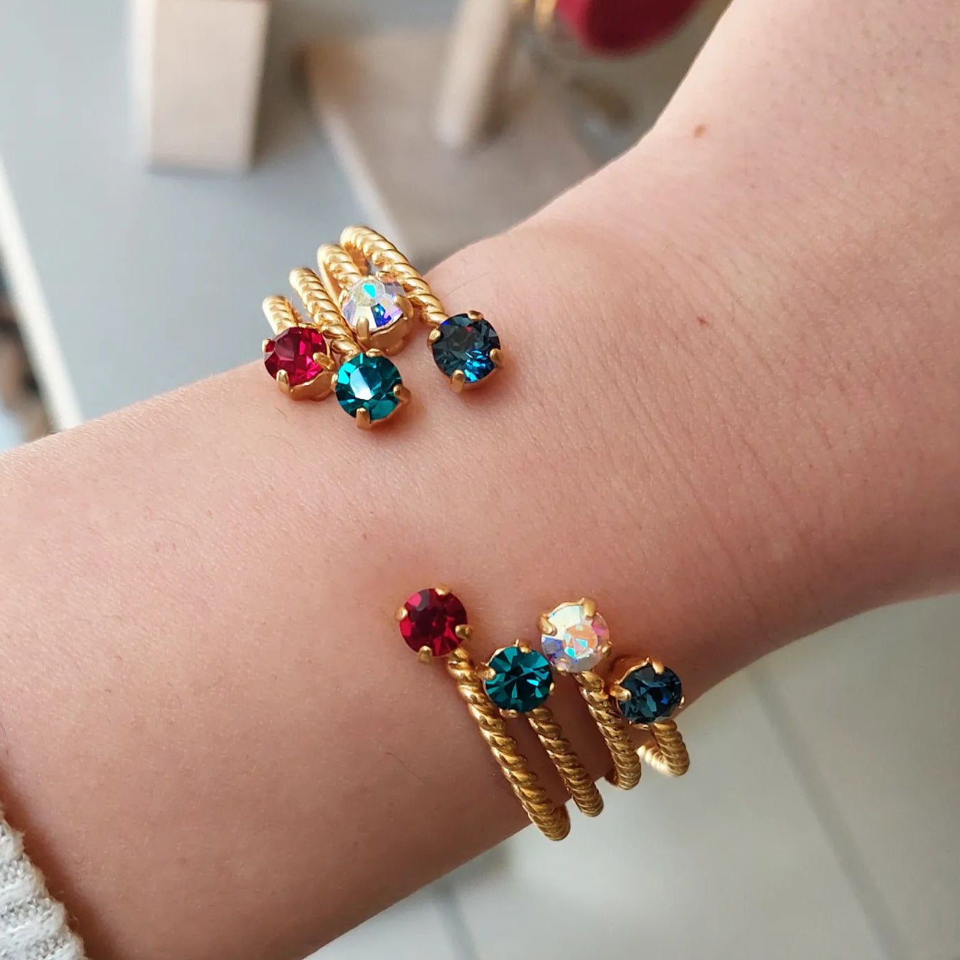 Gold bracelets with colorful gemstones on a wrist against a neutral background