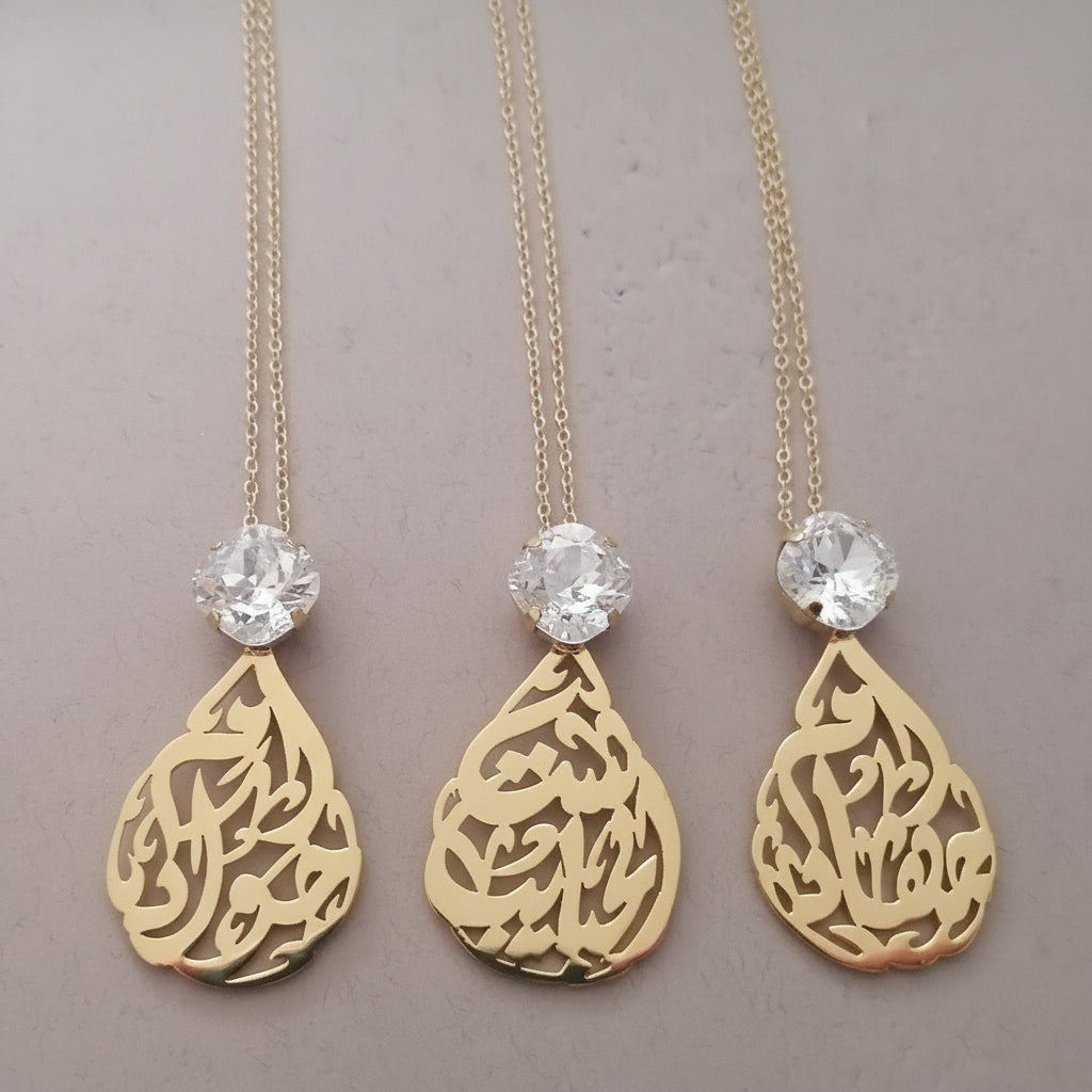 Three gold necklaces with teardrop pendants and crystal beads on a gray background with 'Demirel' branding.