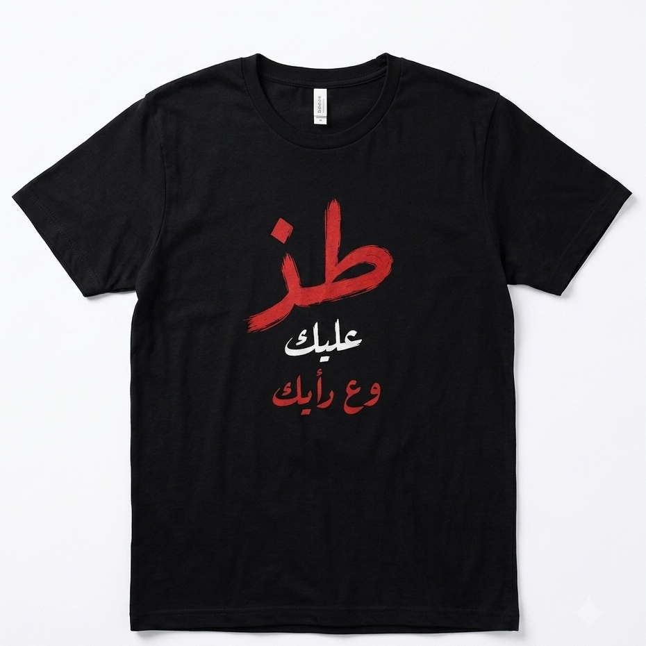 A black short-sleeve crewneck t-shirt with Arabic text printed on the front. The design features a large red Arabic calligraphy character, followed by two lines of white Arabic text, and a bottom line of red Arabic text, all centered on a clean white background. toz 3alek w 3a ra2yak