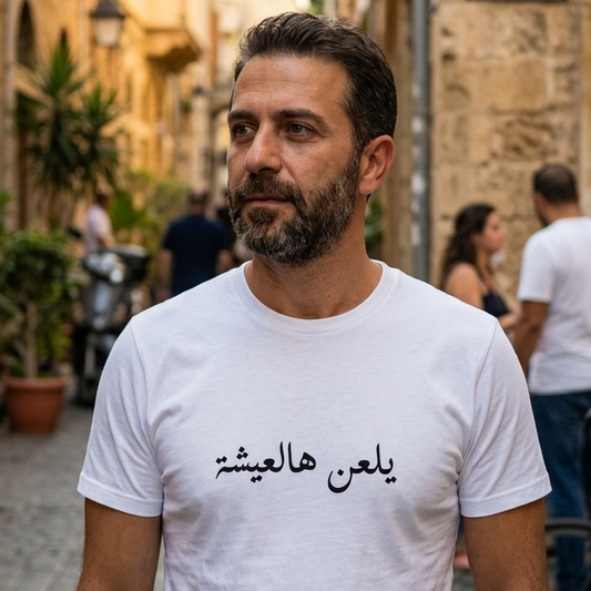 Man wearing a white t-shirt with Arabic text on a street in an urban setting